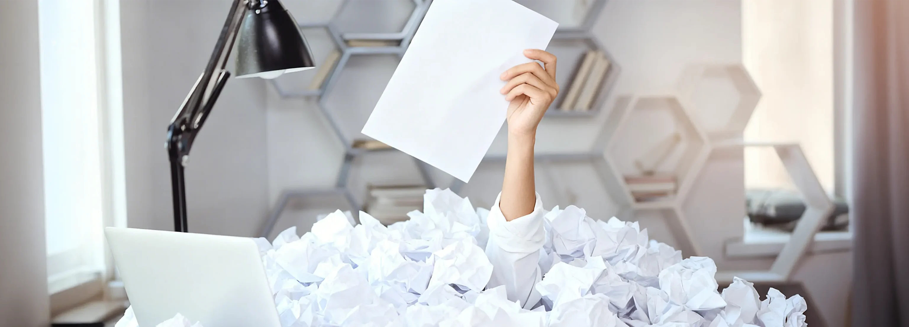 Eine Hand, die ein einzelnes weißes Dokument aus einem Berg von zerknülltem Papier hebt; Metapher für Ordnung im bürokratischen Chaos.